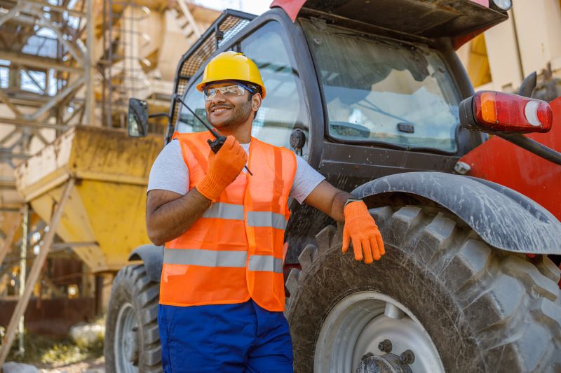 Locação de equipamentos para construção: trabalhador falando ao rádio apoiado em retroescavadeira.